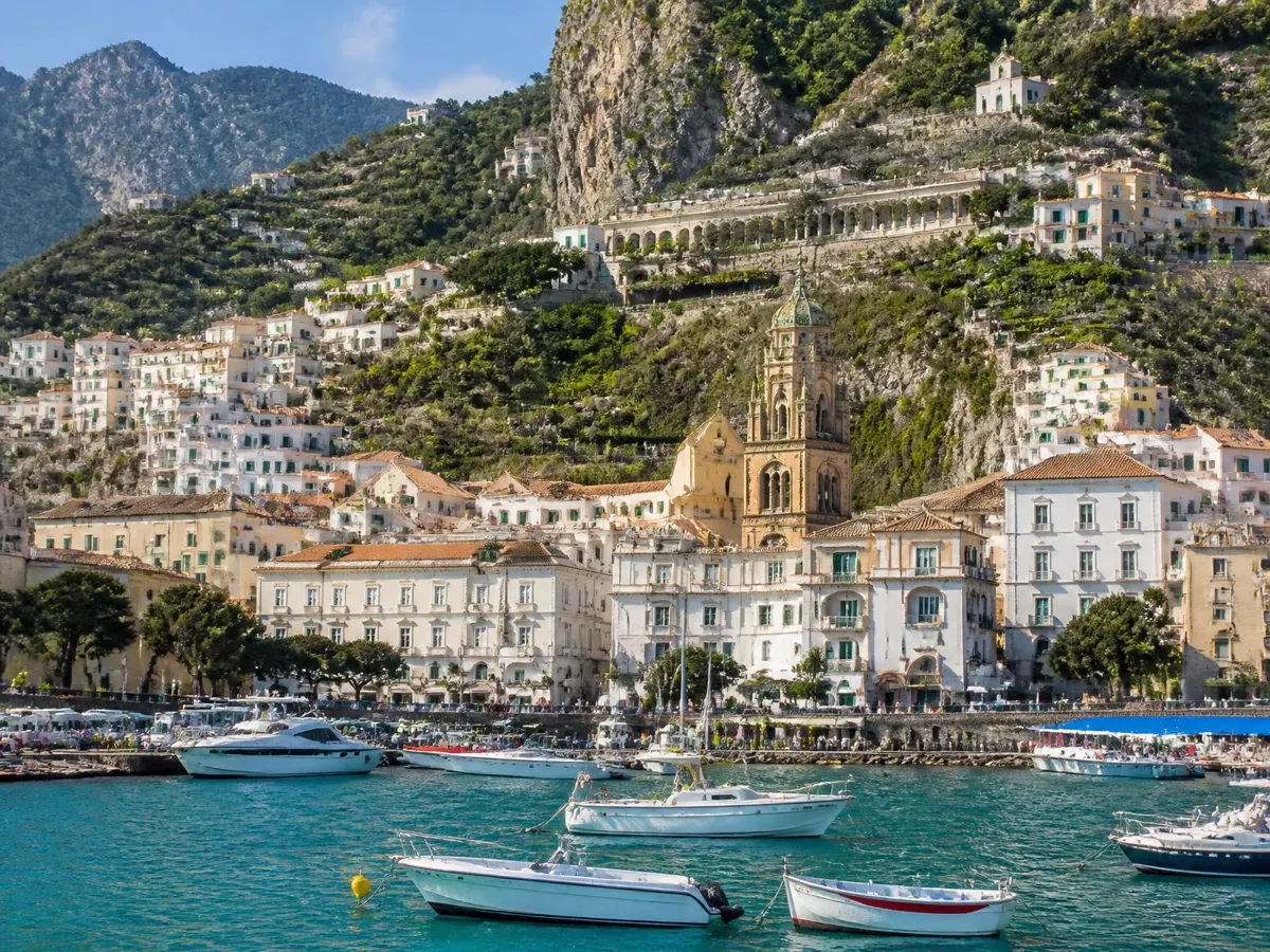 Amalfi vista dal mare: case bianche addossate al vallone, campanile del Duomo e terrazzamenti di limoni