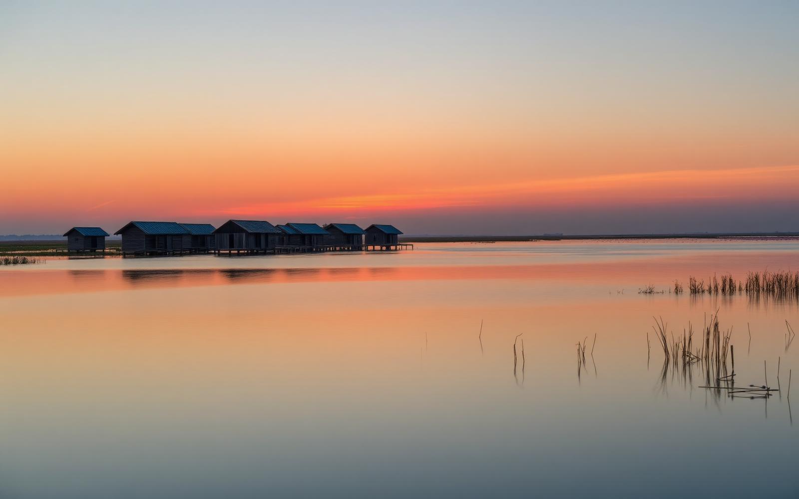 Casoni da pesca in legno nelle valli di Comacchio al tramonto con acque calme